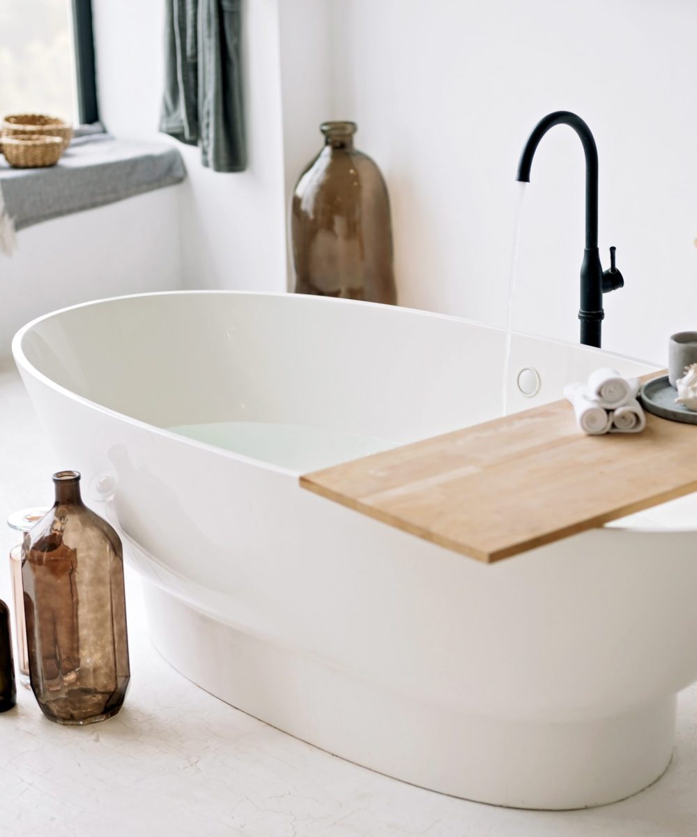 White bathtub fills with foam water in a modern apartment with stylish loft-style interior design, home decor. Spa concept, relaxation. Soft selective focus.